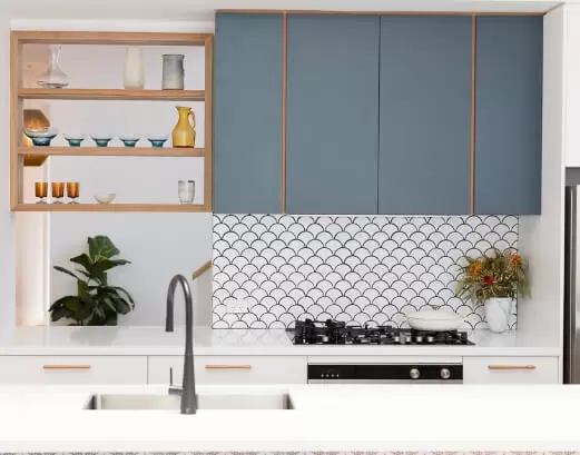 Flat pack kitchen cabinet wall units in matte blue with open wood shelving, scallop tile backsplash, and white countertop.