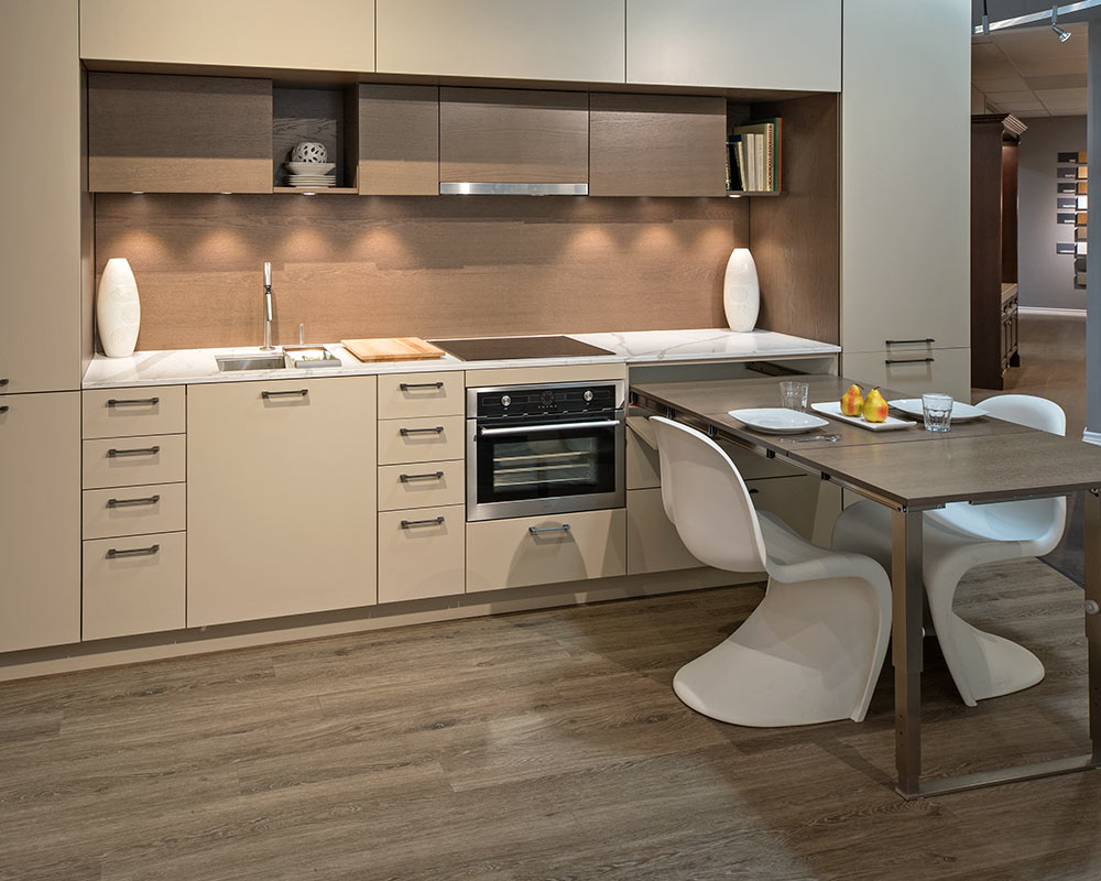 Modern Kitchen cabinet Mississauga design with flat-panel beige cabinets, wood backsplash, under-cabinet lighting, built-in oven, and an integrated dining table.