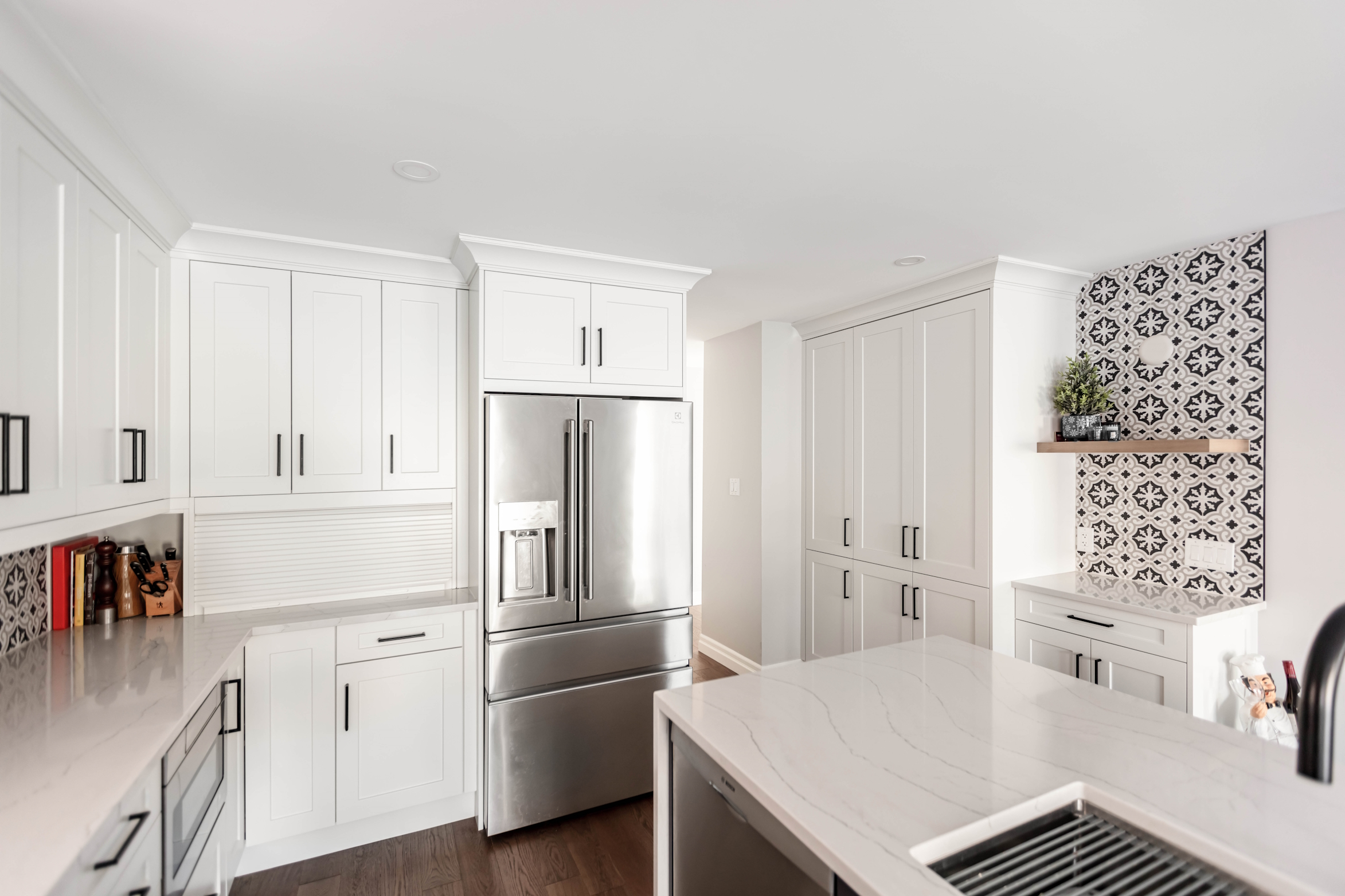 Premade kitchen cabinet set in a bright modern kitchen with white shaker doors, matte black handles, a stainless steel French-door fridge, and a quartz island countertop.
