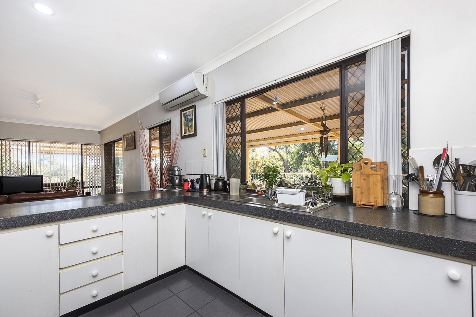 Kitchen suppliers showcase a bright L-shaped kitchen with white cabinets, dark countertops, and a large window.