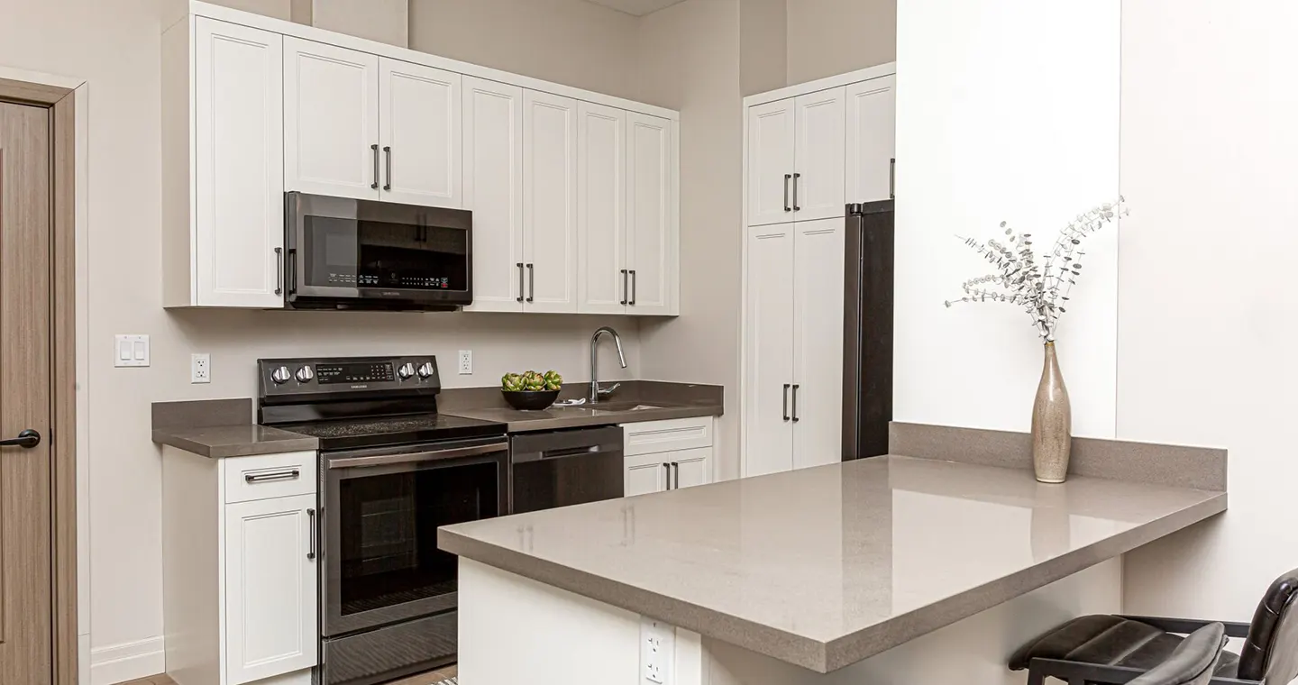Modern white shaker kitchen with grey quartz countertops and island, showcasing storage solutions from KITCHEN SUPPLIERS.