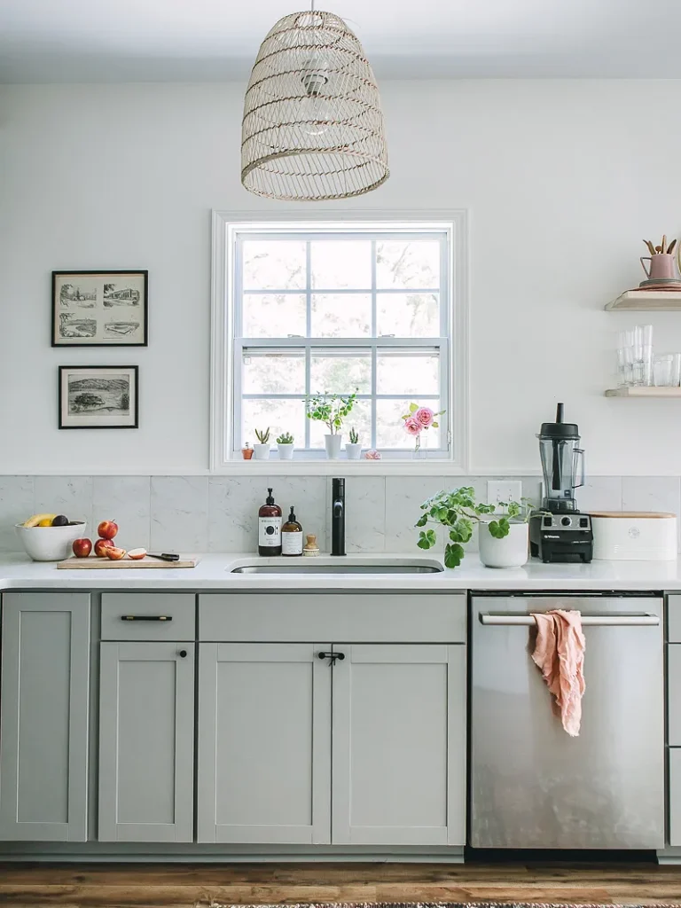Low price kitchen cabinets in gray shaker style with white countertop and sink under a window.