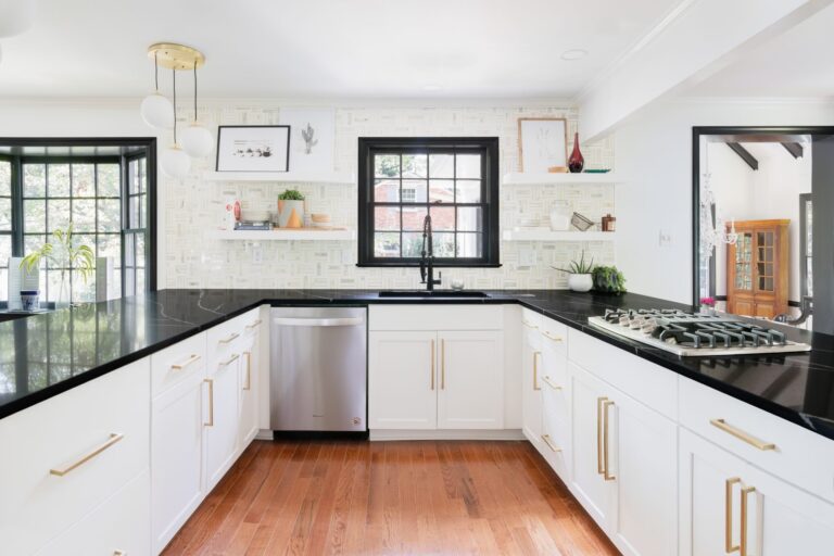 Modern U-shaped kitchen with white shaker premade kitchen cabinet units, black quartz countertops, brass hardware, and a black-framed window above the sink.