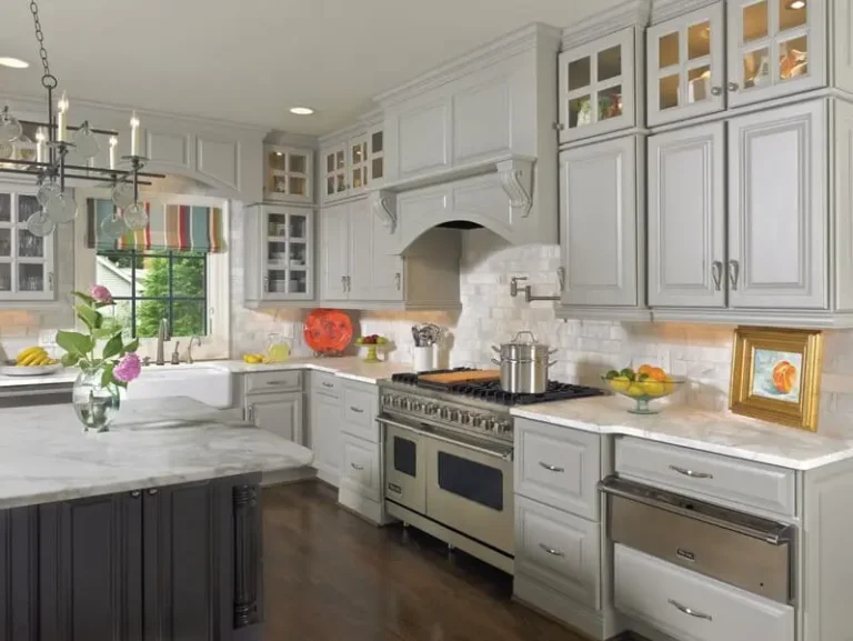 Premade kitchen cabinet setup in a bright modern kitchen with light gray shaker doors, glass-front upper cabinets, marble-look countertops, a dark island, and a professional stainless steel range.