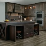 Dark wood premade kitchen cabinet set with X-panel doors, glass uppers, built-in double oven, and a large island with seating.
