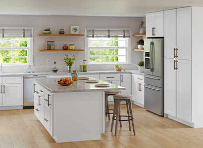 Premade kitchen cabinet set in a bright white shaker kitchen with a large island, quartz-style countertop, and stainless fridge.