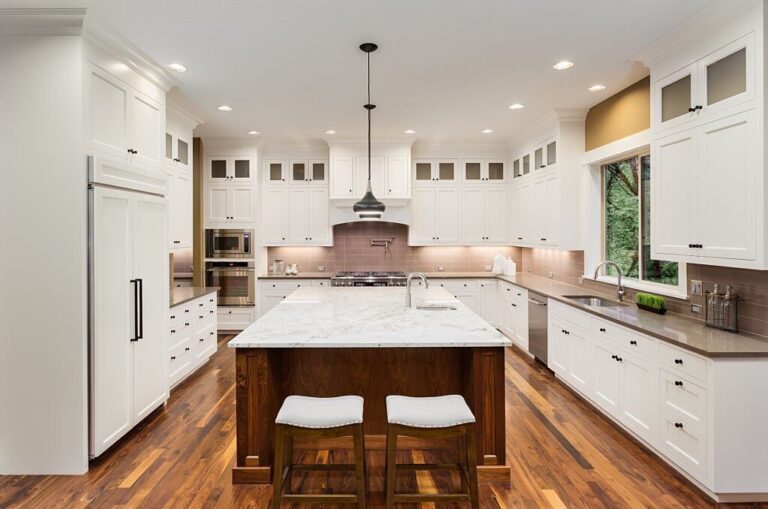 Modern white kitchen cabinets with a large island, quartz countertops, and recessed lighting in a spacious kitchen.