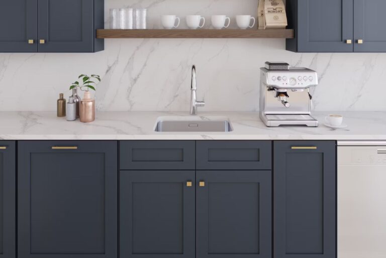 Modern kitchen cabinet supplier display featuring navy shaker cabinets, gold hardware, white marble backsplash, and a sleek countertop with sink and coffee machine.
