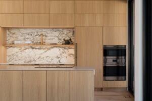 handleless light wood kitchen cabinets with slab doors and marble backsplash