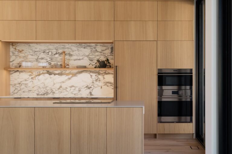 handleless light wood kitchen cabinets with slab doors and marble backsplash