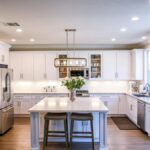 Modern bright kitchen with white shaker premade kitchen cabinet set, large island, stainless steel appliances, and recessed lighting.