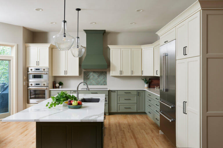 Modern two-tone kitchen cabinets with cream upper cabinets, sage green base cabinets, a quartz island, and stainless steel appliances.