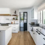 Bright modern white shaker kitchen with black hardware, quartz island, and patterned backsplash by KITCHEN SUPPLIERS.