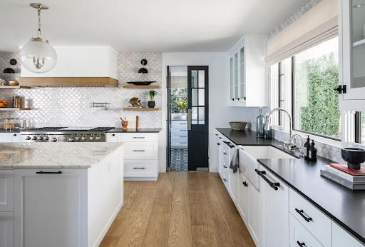 Bright modern white shaker kitchen with black hardware, quartz island, and patterned backsplash by KITCHEN SUPPLIERS.