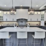 Modern two-tone kitchen with white upper cabinets, dark gray island cabinetry, quartz countertops, and pendant lighting by a kitchen cabinet supplier.