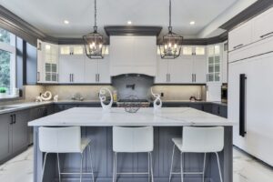 Modern two-tone kitchen with white upper cabinets, dark gray island cabinetry, quartz countertops, and pendant lighting by a kitchen cabinet supplier.