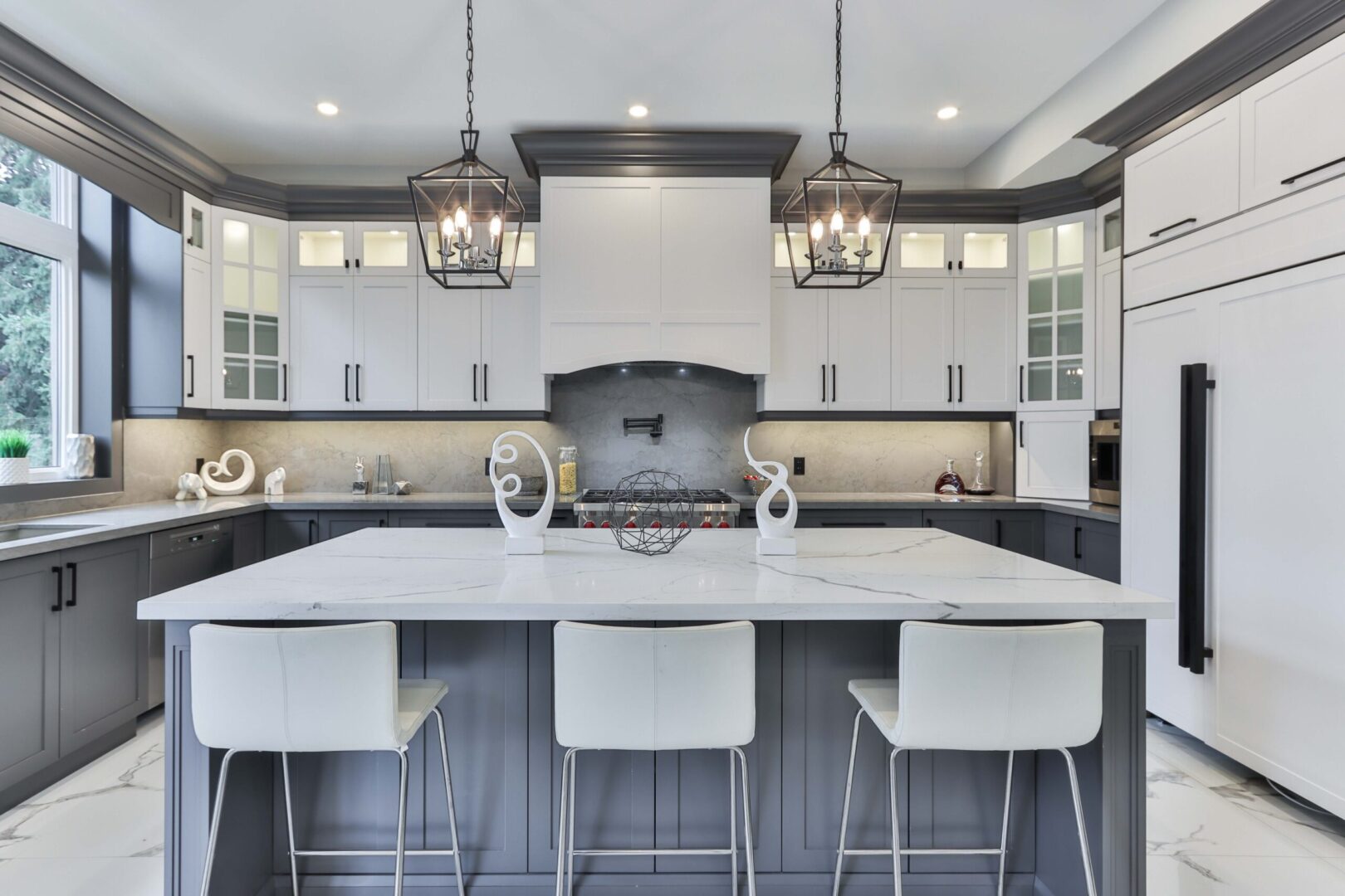 Modern two-tone kitchen with white upper cabinets, dark gray island cabinetry, quartz countertops, and pendant lighting by a kitchen cabinet supplier.