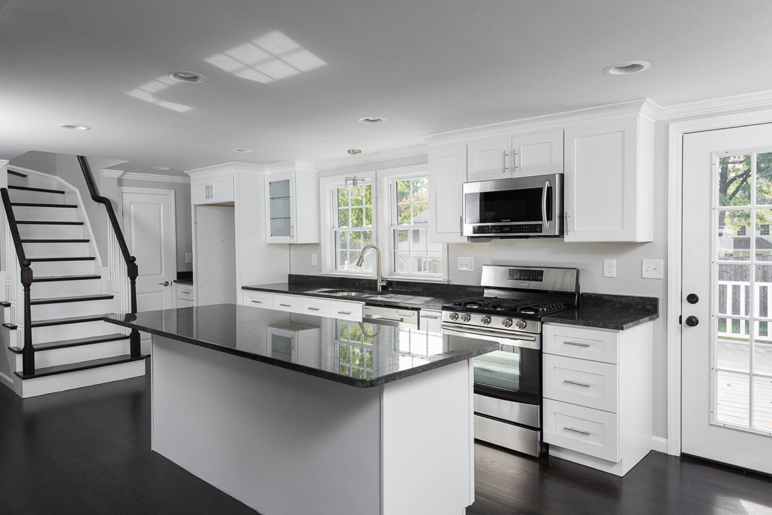 Modern white shaker-style Kitchen Cabinets Vaughan design with black countertops, large island, and stainless steel appliances