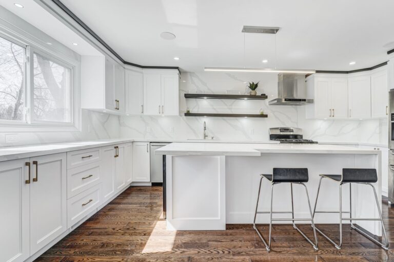 Modern white Kitchen Cabinets Etobicoke design with shaker-style cabinetry, brass hardware, waterfall island, open shelving, and dark wood flooring.