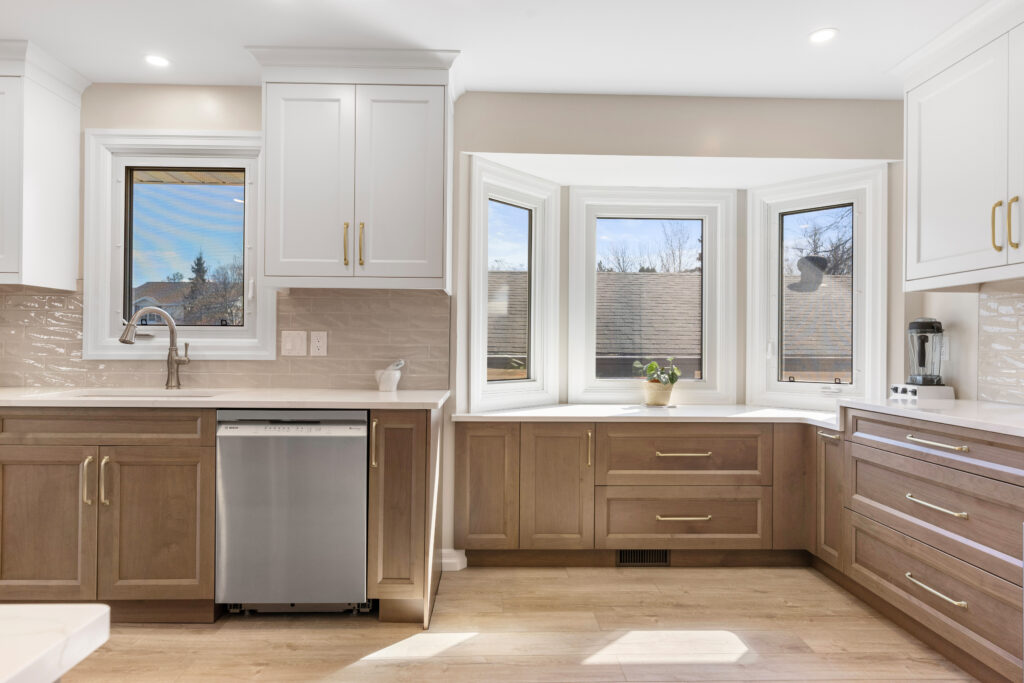 Modern kitchen cabinets in a bright U-shaped kitchen with white upper cabinets, wood lower cabinets, and large bay windows