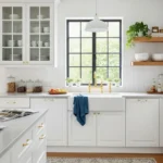 Bright modern kitchen cabinets in white with glass-front uppers, gold hardware, open wood shelves, and large black-framed windows