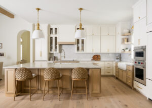 Bright modern kitchen with white and natural wood kitchen cabinets, a large island, brass hardware, and woven bar stools.