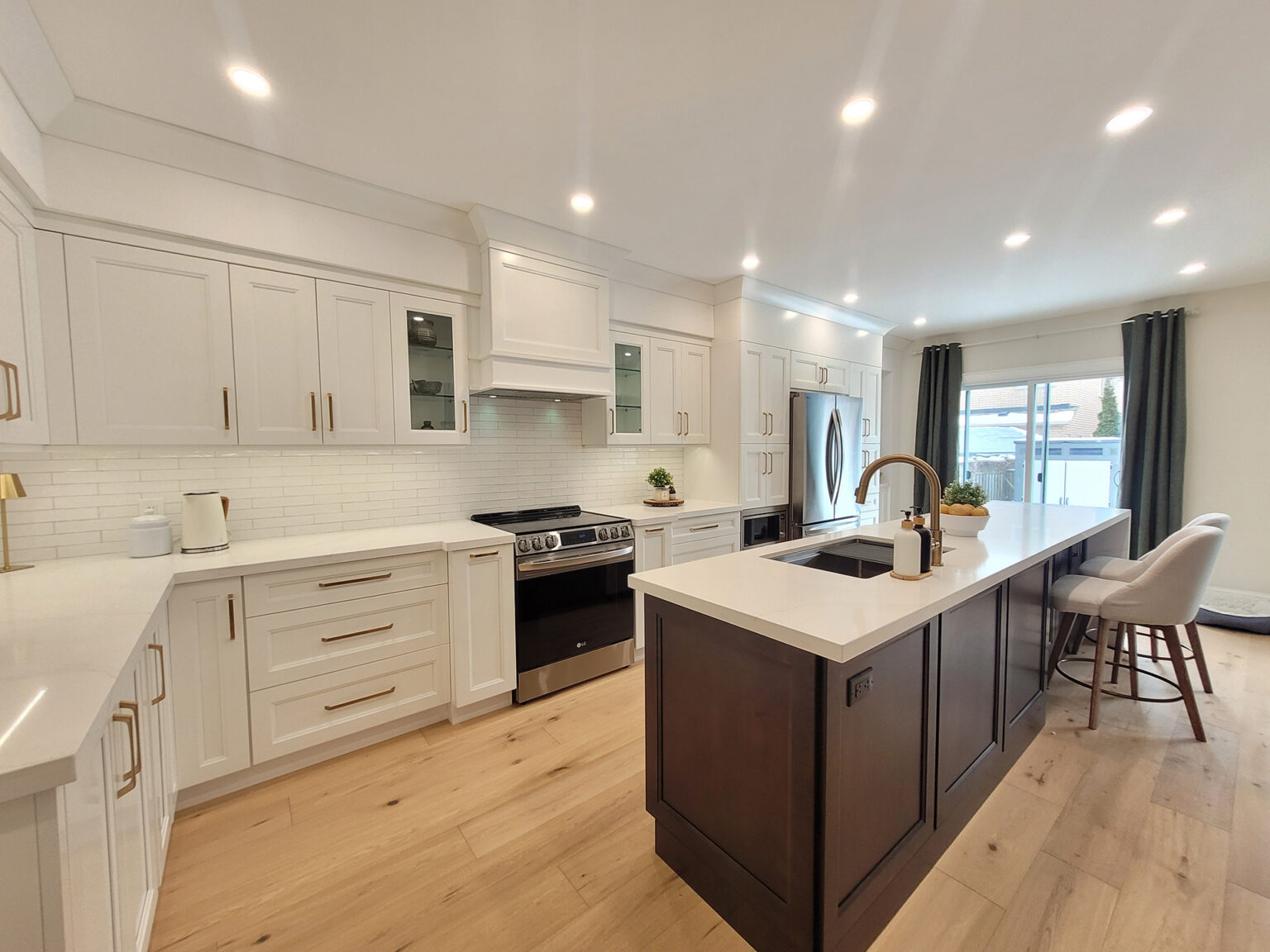 Kitchen cabinets Mississauga in a bright two-tone kitchen with white Shaker cabinetry, brass pulls, a dark island, and white quartz countertops.