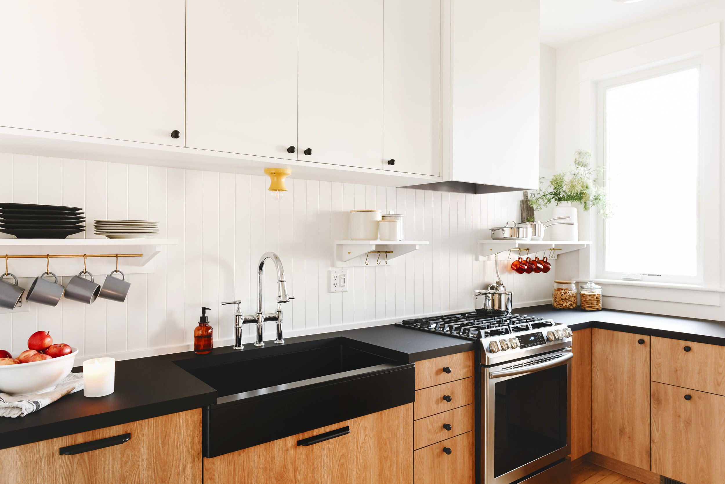Modern IKEA kitchen cabinets with white upper cabinets, natural wood lower cabinets, black countertops, and a farmhouse sink