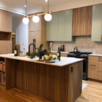 Modern Kitchen Cabinets Burlington design featuring light wood lower cabinets, soft green upper cabinets, a fluted wood island, and white countertops in a bright contemporary kitchen.