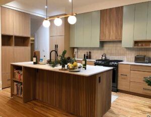 Modern Kitchen Cabinets Burlington design featuring light wood lower cabinets, soft green upper cabinets, a fluted wood island, and white countertops in a bright contemporary kitchen.
