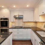 Modern white shaker Kitchen Cabinets Markham with black countertops, stainless steel appliances, recessed lighting, and a bright U-shaped layout.