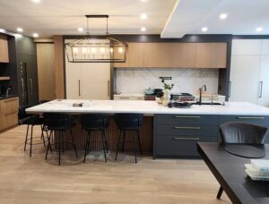 Modern Kitchen Cabinets Etobicoke featuring a large white waterfall island, black lower cabinets, light wood upper cabinetry, and elegant pendant lighting in an open-concept home.