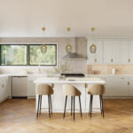 Kitchen Cabinets Burlington in a bright modern kitchen with white shaker cabinetry, gold hardware, large island, and herringbone wood flooring