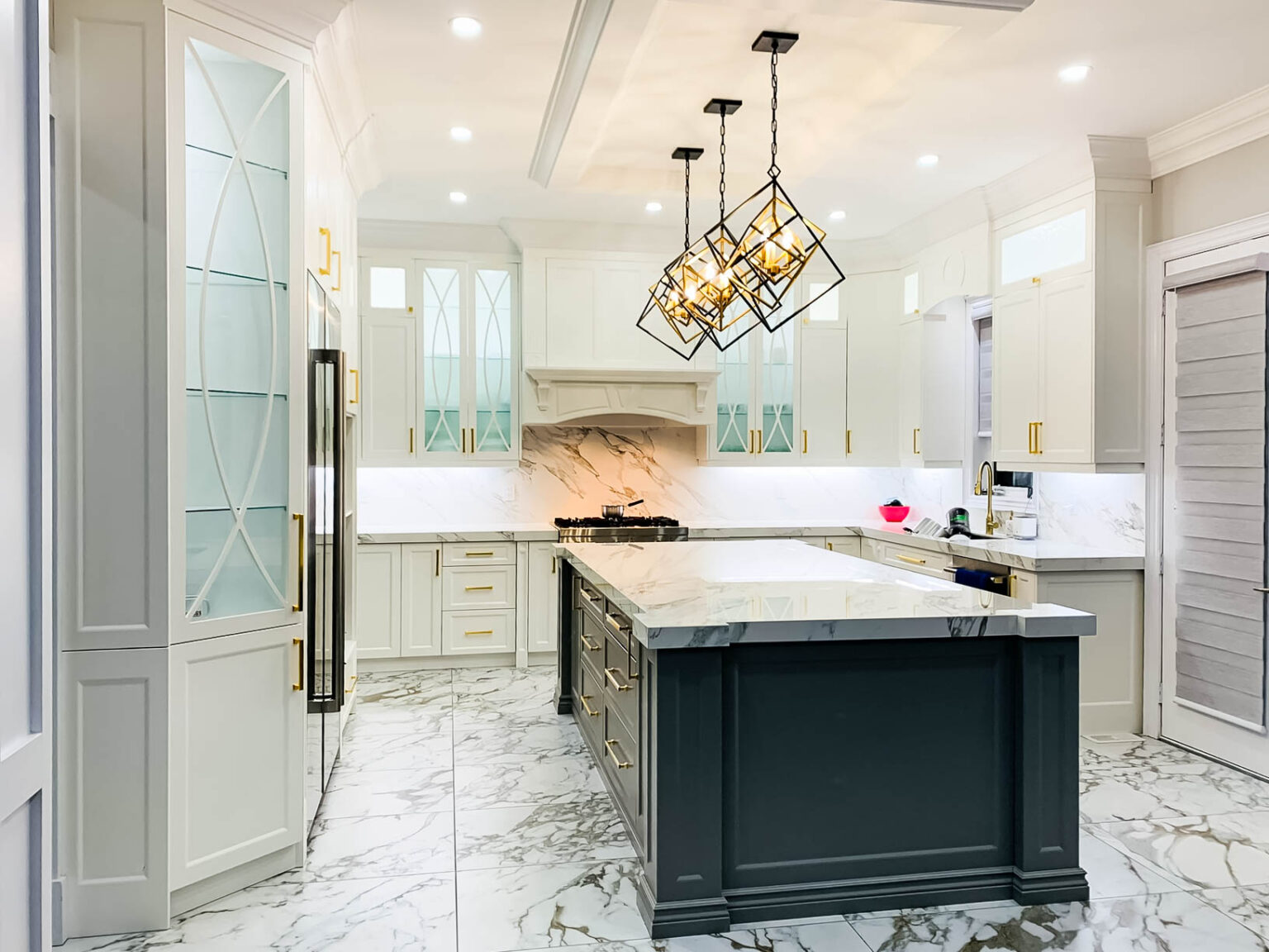 Luxury white kitchen cabinets Mississauga with marble countertops, black island, and modern pendant lighting in an elegant contemporary kitchen.