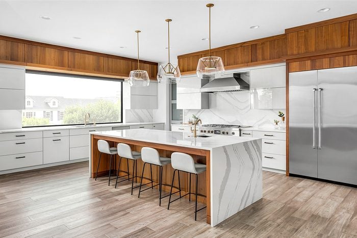 Modern Kitchen Cabinets Vaughan design featuring sleek white cabinetry, warm wood accents, a large waterfall island, pendant lighting, and stainless steel appliances.