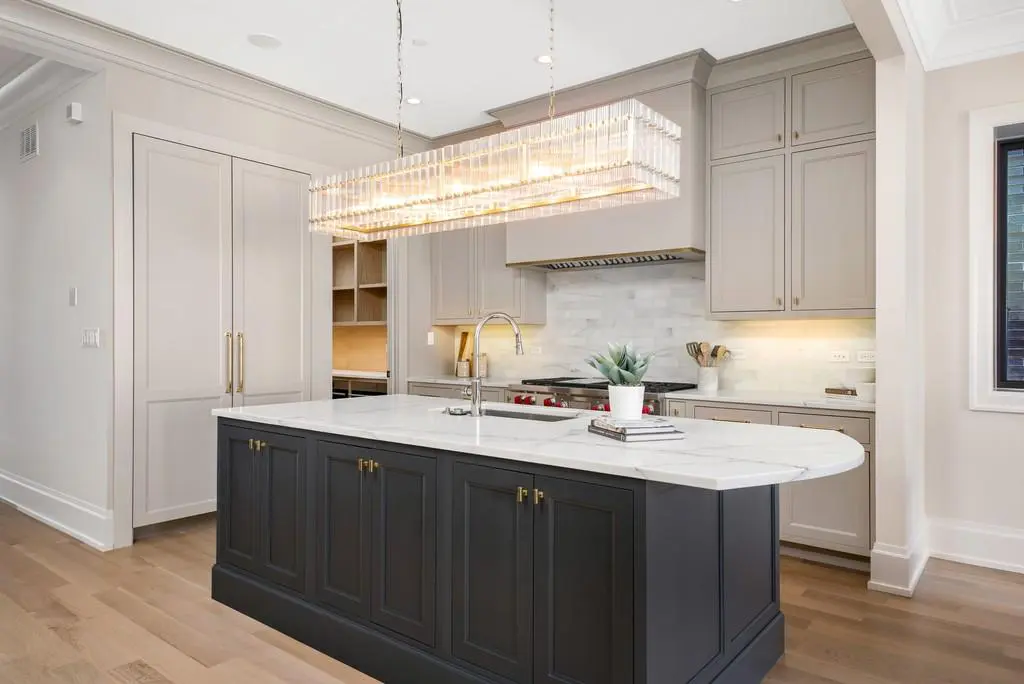 Modern Kitchen Cabinets Toronto featuring light beige perimeter cabinets, a dark navy island, marble countertop, and elegant pendant lighting