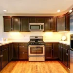 Modern kitchen with dark wood kitchen cabinet doors, stainless steel appliances, and warm lighting in a renovated home.