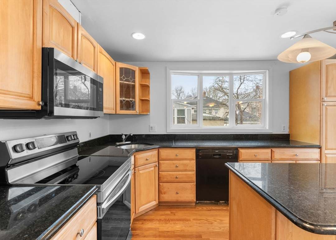 Kitchen Cabinets Milton in a bright modern kitchen with natural wood cabinets, black countertops, and a functional island