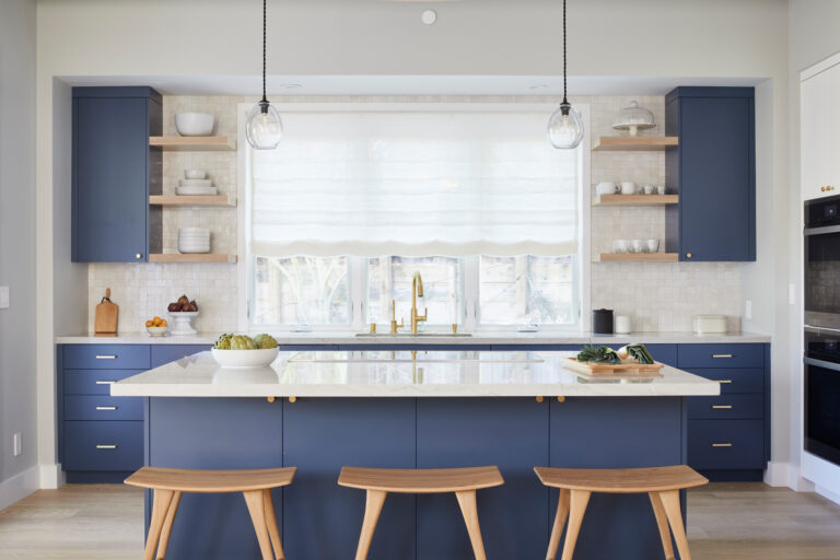 Modern Kitchen Cabinets Burlington design featuring deep blue flat-panel cabinets, a large white waterfall island, open wood shelving, brass fixtures, and three wood bar stools in a bright contemporary kitchen.