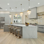 Modern Kitchen Cabinets Hamilton design featuring light gray cabinets, a large white waterfall island, brass bar stools, and elegant pendant lighting in a bright open-concept kitchen.