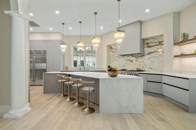 Modern Kitchen Cabinets Hamilton design featuring light gray cabinets, a large white waterfall island, brass bar stools, and elegant pendant lighting in a bright open-concept kitchen.