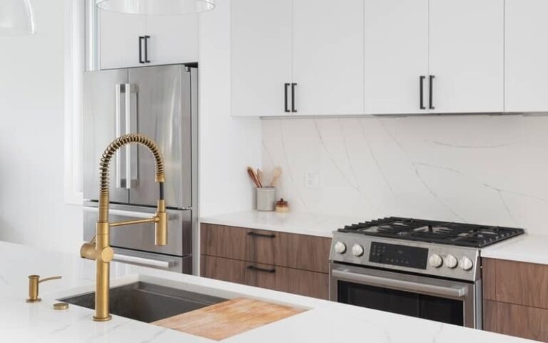 Glossy white cabinets in a modern kitchen with wood base cabinets, stainless appliances, and a gold faucet
