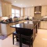 Modern kitchen cabinets Mississauga home featuring cream raised-panel cabinetry, a large dark island, stainless steel appliances, and a tile backsplash.