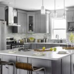 Modern gray shaker kitchen cabinets Mississauga with a large white island, stainless steel appliances, pendant lighting, and tile backsplash.