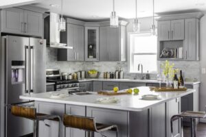 Modern gray shaker kitchen cabinets Mississauga with a large white island, stainless steel appliances, pendant lighting, and tile backsplash.