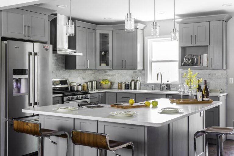 Modern gray shaker kitchen cabinets Mississauga with a large white island, stainless steel appliances, pendant lighting, and tile backsplash.