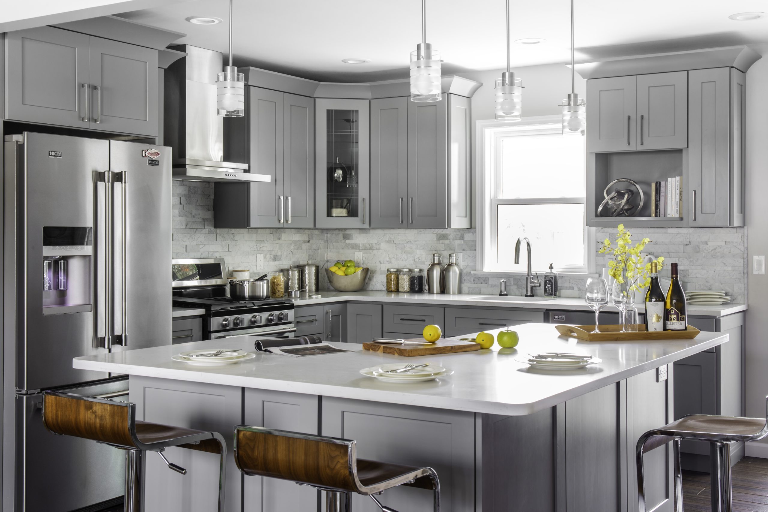 Modern gray shaker kitchen cabinets Mississauga with a large white island, stainless steel appliances, pendant lighting, and tile backsplash.