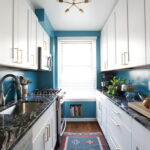 White shaker kitchen cabinets Mississauga in a bright galley kitchen with brass handles, blue walls, and dark marble countertops