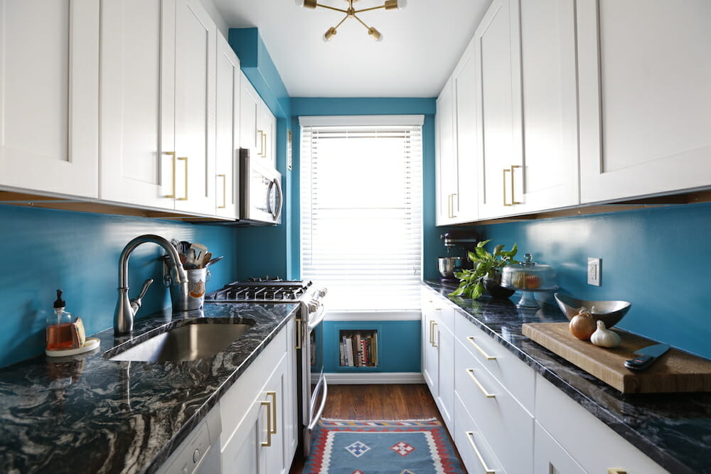 White shaker kitchen cabinets Mississauga in a bright galley kitchen with brass handles, blue walls, and dark marble countertops
