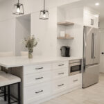 kitchen cabinets Mississauga – modern white shaker cabinets with large island, black handles, and stainless steel fridge